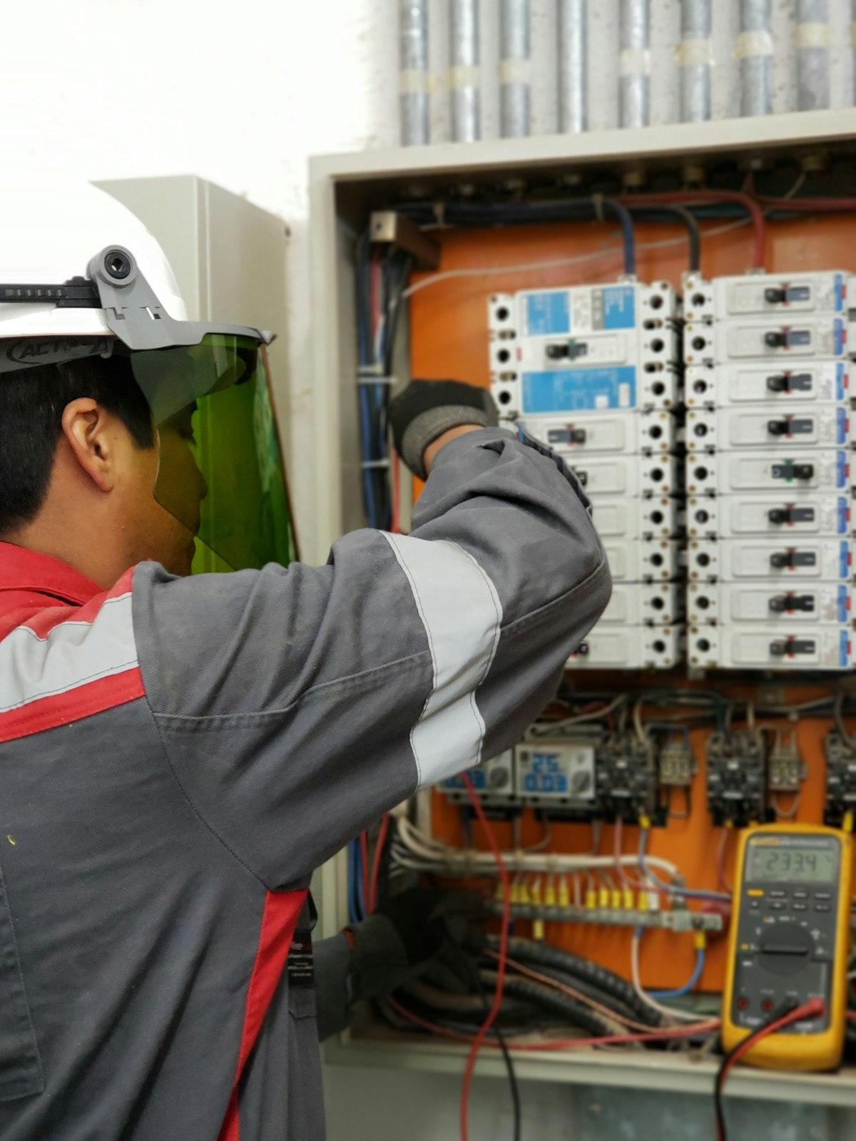 Electrician in protective gear testing an electrical panel